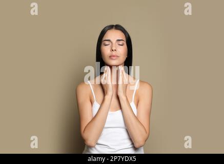 Giovane donna che fa l'auto-esame della tiroide su sfondo beige Foto Stock