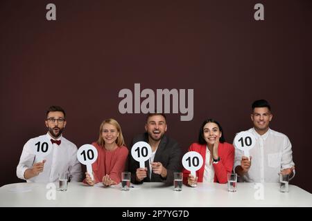 Gruppo di giudici che tiene i segni con il punteggio più alto a tavola su sfondo marrone Foto Stock