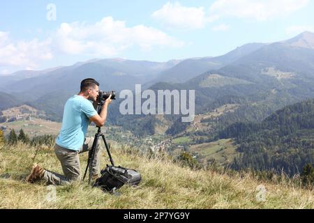 Uomo che scatta foto del paesaggio montano con una fotocamera moderna su un cavalletto all'aperto Foto Stock