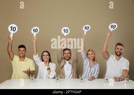 Gruppo di giudici che tiene i segni con il punteggio più alto a tavola su sfondo beige Foto Stock