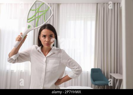 Giovane donna con mosca elettrica swatter in interni. Insetto killer Foto Stock