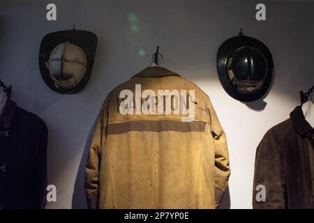 Un cappotto di pompieri etichettato Hampton è appeso su una volontà con caschi antincendio che lo circondano nel Seacoast Fire Museum presso il Tuck Museum of Hampton History. H Foto Stock