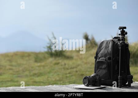 Zaino, fotocamera, cavalletto e computer portatile del fotografo su superfici in legno all'aperto. Spazio per il testo Foto Stock