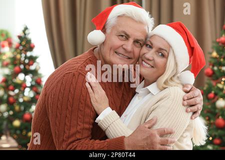 Felice coppia matura in cappelli di Santa a casa. Festa di Natale Foto Stock