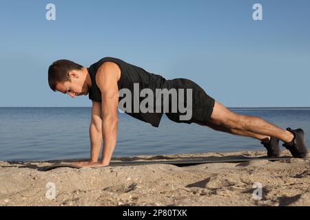 Uomo sportivo che fa esercizio su una tavola a braccio dritto in spiaggia Foto Stock