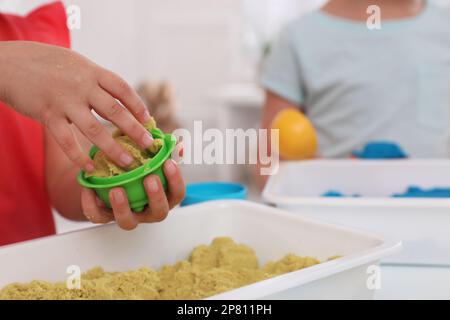 Bambini piccoli che giocano con sabbia cinetica luminosa al tavolo al coperto, primo piano Foto Stock