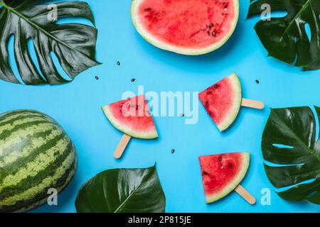 Deliziosi cocomeri maturi e foglie tropicali su sfondo azzurro, piatto Foto Stock