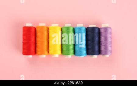 Diversi fili da cucire su fondo rosa, giacitura piatta Foto Stock