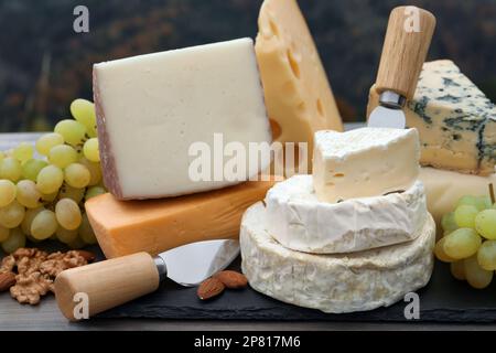 Diversi tipi di deliziosi formaggi e snack su tavola di legno all'aperto Foto Stock