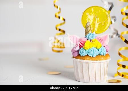 Cupcake dolce carino unicorno con lollipop giallo sul tavolo bianco, spazio per il testo. Festa Foto Stock