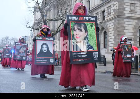 Londra, Regno Unito. 8th marzo, 2023. Donne anglo-iraniane vestite di mantello ispirate ai personaggi di Magaret Atwood's, 'The Haindmaid's tale'. La marcia che si è svolta per sostenere le donne in Iran ha proseguito silenziosamente lungo Whitehall, mentre i partecipanti portavano un ritratto di qualcuno che è stato ucciso o imprigionato dal regime islamico dal settembre dello scorso anno. Credit: Undicesima ora di Fotografia/Alamy Live News Foto Stock