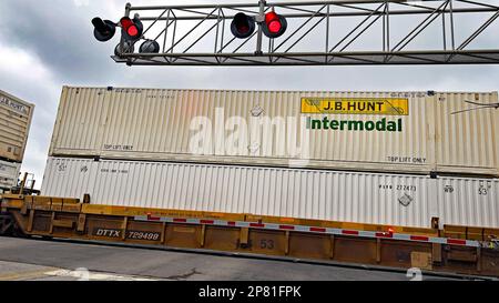 EMPORIA, KANSAS - 8 MARZO 2023 Un treno merci intermodale BNSF che trasporta scatole di carico per J.B. Hunt passa sotto i semafori di sicurezza e supera la barra di attraversamento che ferma il traffico sull'incrocio commerciale Foto Stock