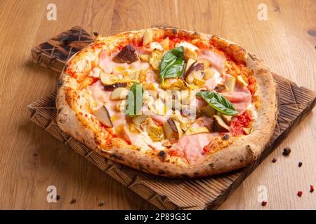 Pizza Capricciosa con formaggio, pancetta, pomodori, funghi e basilico, pasto italiano. Pizza napoletana al forno con carciofi servita su tavola di legno. Foto Stock