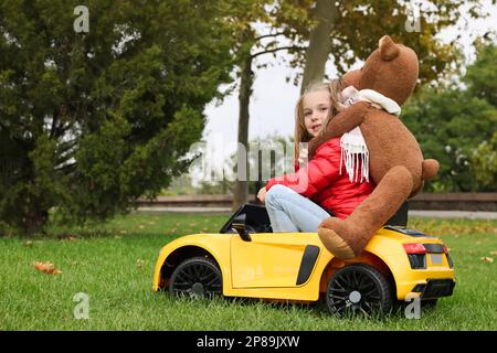 Ragazza carina con orso giocattolo che guida l'auto per bambini nel parcheggio. Spazio per il testo Foto Stock