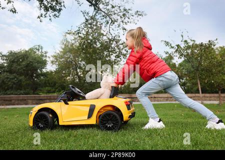 Carina bambina che gioca con l'orso giocattolo e l'auto per bambini nel parcheggio Foto Stock