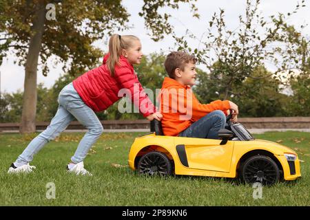 Ragazza carina che spinge l'auto dei bambini con il bambino in parcheggio Foto Stock