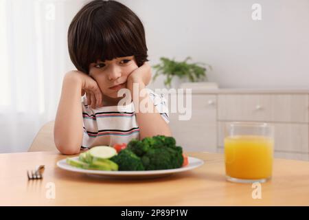 Carino ragazzino che si rifiuta di mangiare verdure a casa Foto Stock