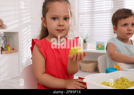 I bambini piccoli cute che giocano con sabbia cinetica luminosa al tavolo in camera Foto Stock