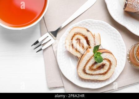 Gustoso rotolo di torta con marmellata e tazza di tè su tavolo di legno bianco, piatto Foto Stock