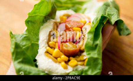 Hummus su una foglia di insalata con mais e ravanello. Foto Stock