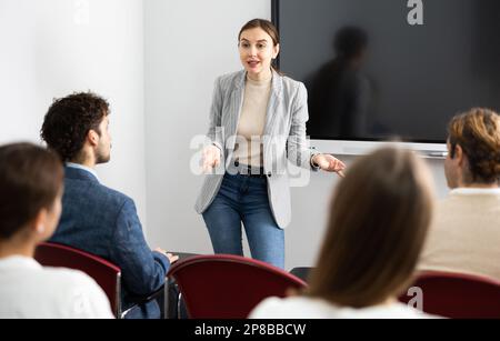 Una coach femminile qualificata e positiva che spiega l'argomento a un gruppo di persone durante una lezione di lingua straniera nell'auditorio Foto Stock