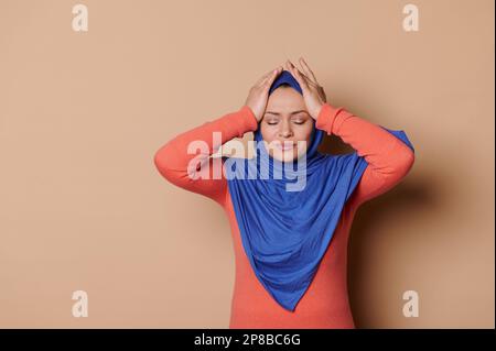 Donna musulmana in hijab, strofinando templi, curare mal di testa tensione, soffre di emicaina, dolore, sfondo beige Foto Stock