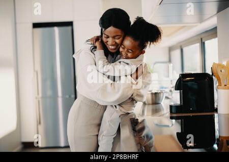 Ti amo mamma, bambina abbraccia la mamma in cucina. Madre e figlia celebrano la giornata della madre in abiti coordinati. Amore tra una madre Foto Stock