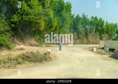 Un uomo di villaggio a piedi accanto alla strada in giorno di sole Foto Stock