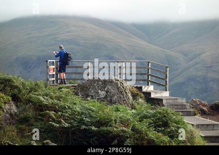 Uomo che fotografi sulla piattaforma di osservazione in legno sul Wainwright "Raven Crag" Thirlmere nel Lake District National Park, Cumbria, Inghilterra, Regno Unito. Foto Stock