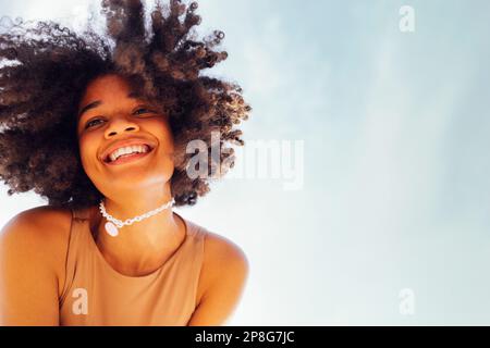 Primo piano ritratto di felice ragazza afro-americana sorridente dolcemente alla fotocamera. Ragazza nera mista razza con capelli afro ricci. Ridendo te Foto Stock