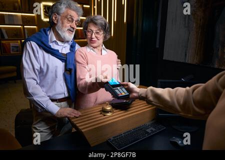 L'uomo e la donna anziani lasciano l'albergo e pagano il loro soggiorno Foto Stock