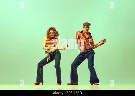 Sensazione di ritmo. Coppia gente felice, uomo e donna in stile retrò abiti danza discoteca danza su sfondo verde. Concetto di moda 1970s, 1980s Foto Stock