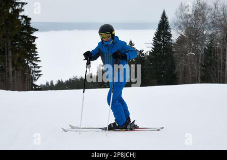 Un uomo con abbigliamento sportivo blu sugli sci si trova sullo sfondo di una pista innevata Foto Stock