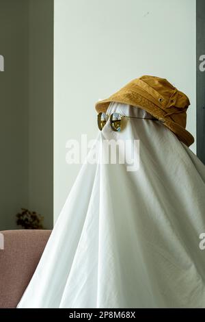 Una persona che indossa un cappello e occhiali da sole neri su un panno bianco che assomiglia a un fantasma Foto Stock