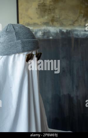 Una persona che indossa un cappello e occhiali da sole neri su un panno bianco che assomiglia a un fantasma Foto Stock