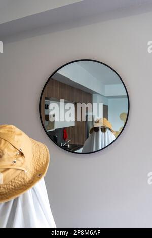 Una persona che indossa un cappello e occhiali da sole con la montatura nera su un panno bianco che assomiglia a un fantasma che guarda in uno specchio Foto Stock