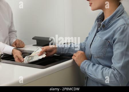 Donna che dà denaro al cassiere in banca, primo piano. Cambio valuta Foto Stock