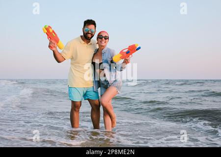 Felice coppia con pistole ad acqua in mare al tramonto Foto Stock