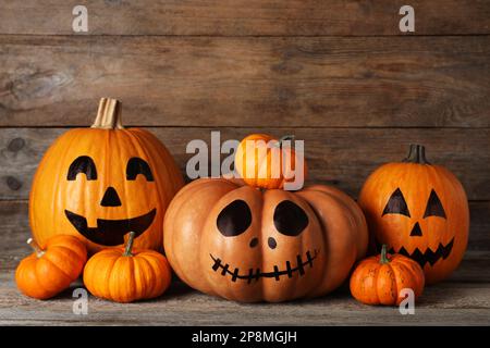 Zucche arancioni e tre con facce spoky disegnate sul tavolo di legno. Festa di Halloween Foto Stock