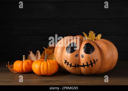 Zucche arancioni e una con la faccia spoky disegnata sul tavolo di legno. Festa di Halloween Foto Stock