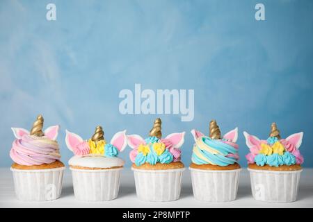 Molti dolci cupcakes unicorno carino su tavolo di legno bianco contro sfondo azzurro Foto Stock