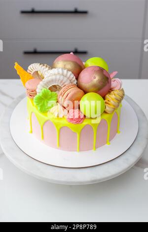 Verde neon, lime e rosa flebo torta di compleanno felice sormontata con fiori assortiti di cioccolato color arcobaleno, palle, meringhe e caramelle Foto Stock