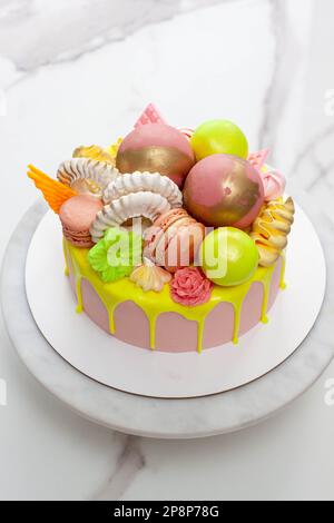 Verde neon, lime e rosa flebo torta di compleanno felice sormontata con fiori assortiti di cioccolato color arcobaleno, palle, meringhe e caramelle Foto Stock