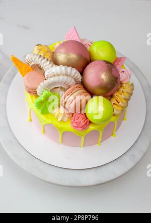 Verde neon, lime e rosa flebo torta di compleanno felice sormontata con fiori assortiti di cioccolato color arcobaleno, palle, meringhe e caramelle Foto Stock