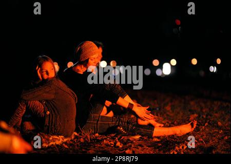 Giovane donna e bambina seduta a terra tra foglie morte, luce del fuoco acceso. In attesa del rituale pagano. Novembre 11, 201 Foto Stock