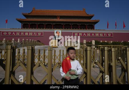 Un ragazzo tiene con la Cina posa bandiera nazionale sotto un ritratto del defunto presidente cinese Mao Zedong vicino polizia e agenti di polizia paramilitare in piedi guardia alla porta Tiananmen, davanti al Congresso nazionale del popolo (NPC) a Pechino, Cina 3 marzo 2023. 03MAR23 SCMP / Robert ng Foto Stock