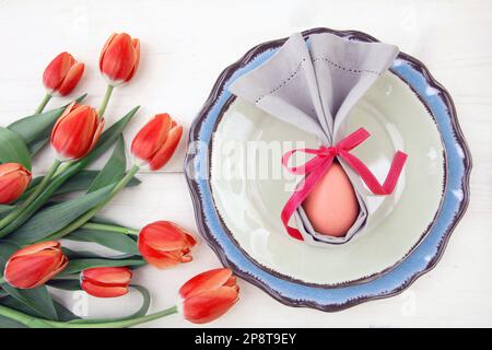 Impostazione e decortazione della tavola di Pasqua, tulipani e uovo di Pasqua in un tovagliolo grigio su piatti set, sfondo bianco Foto Stock