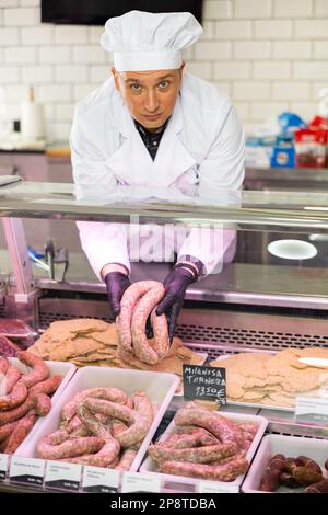 Macellaio maschio positivo con salsiccia di manzo fresca in macelleria Foto Stock