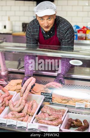 Macellaio maschio positivo con salsiccia di manzo fresca in macelleria Foto Stock