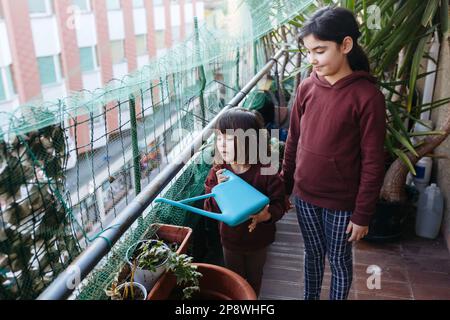 vista ad angolo alto su due bambini sul balcone dell'appartamento che innaffia le piante nelle pentole Foto Stock